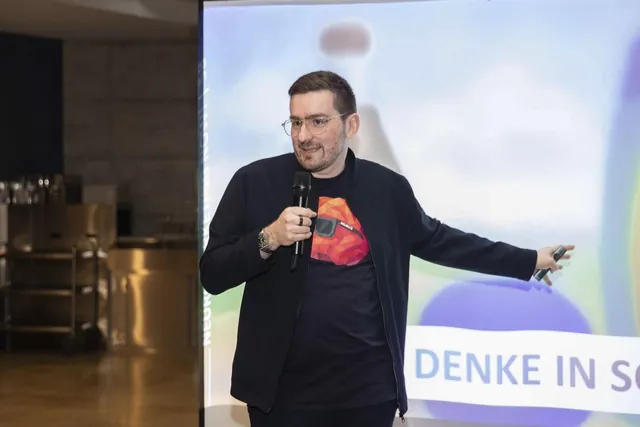 Christian Dietz mit Mikrofon zeigt auf die Leinwand